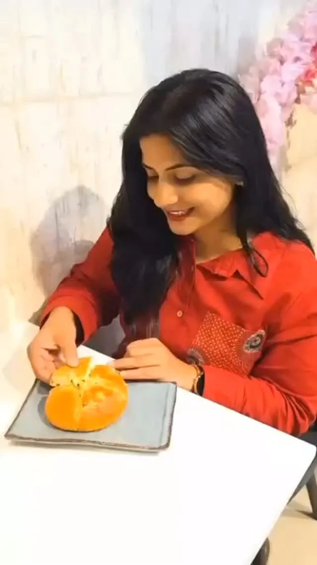 A guest in a red shirt at a café table breaking open a golden cheese-filled Korean bun on a grey plate.